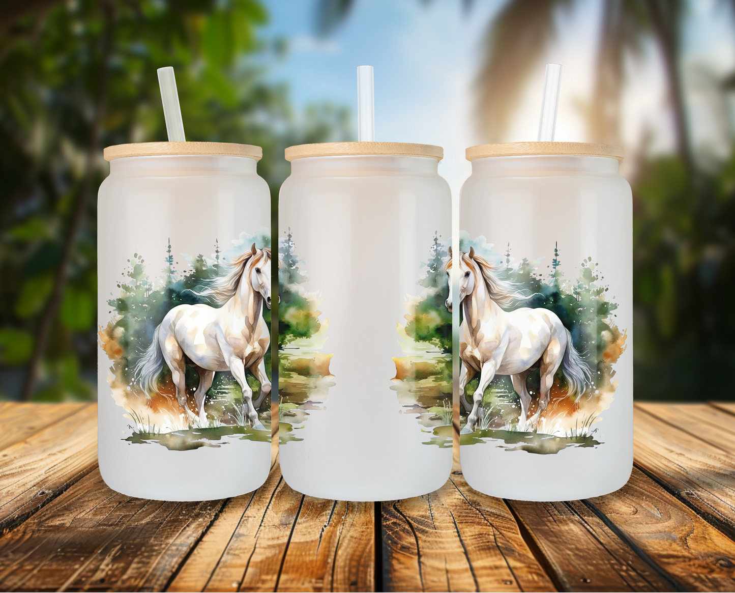 Three frosted glass cans with a white horse design, displayed on a wooden table against a tropical backdrop, each topped with a bamboo lid and clear straw.